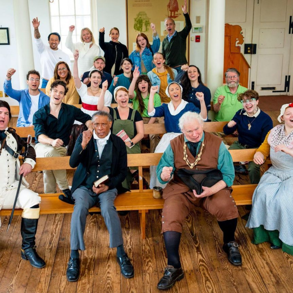 A group of costumed History Makers sitting on benches during staff training at the Benstitute