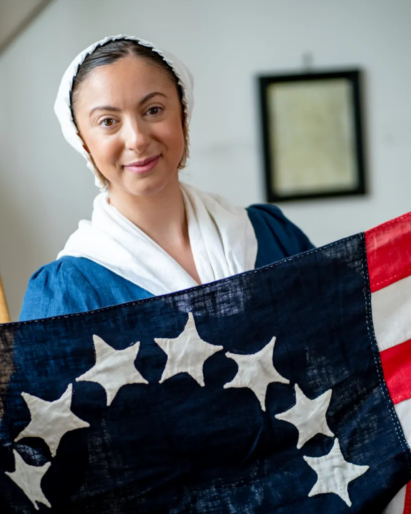 A History Maker portraying Betsy Ross poses with an early version of the US flag
