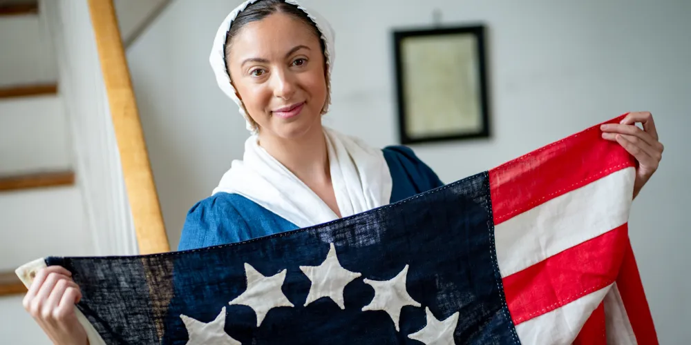 A History Maker portraying Betsy Ross poses with an early version of the US flag