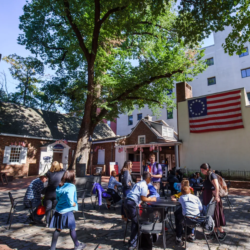 People gather around tables in the outside courtyard of the Betsy Ross House