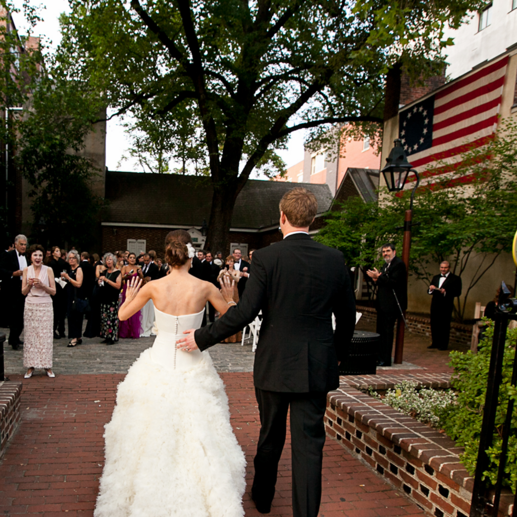 A bride and groom arrive to a crowd of wedding guests in the Betsy Ross House courtyard
