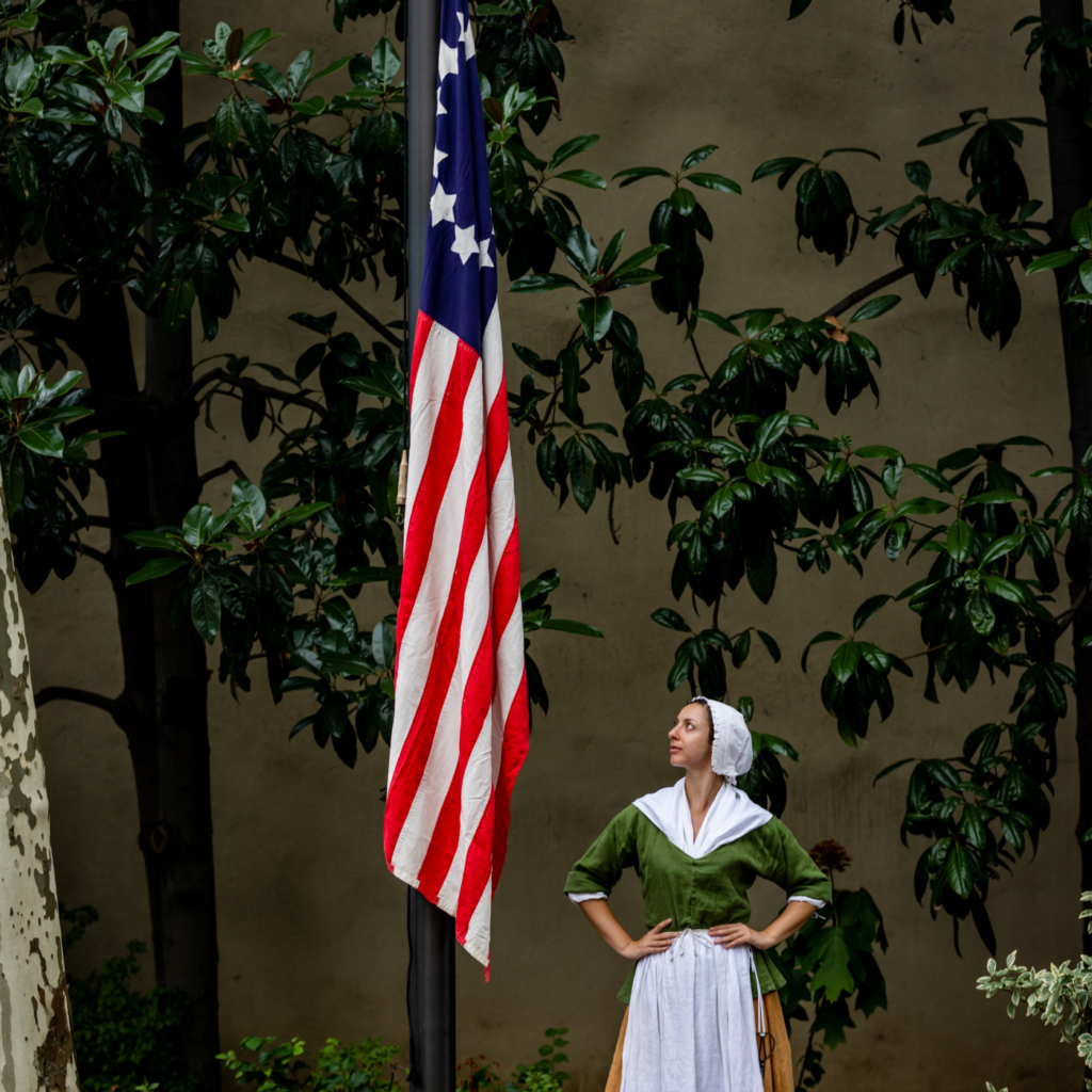 在贝齐·罗斯故居的庭院里，一位扮演贝齐·罗斯的历史人物雕塑站在一面早期美国国旗旁。