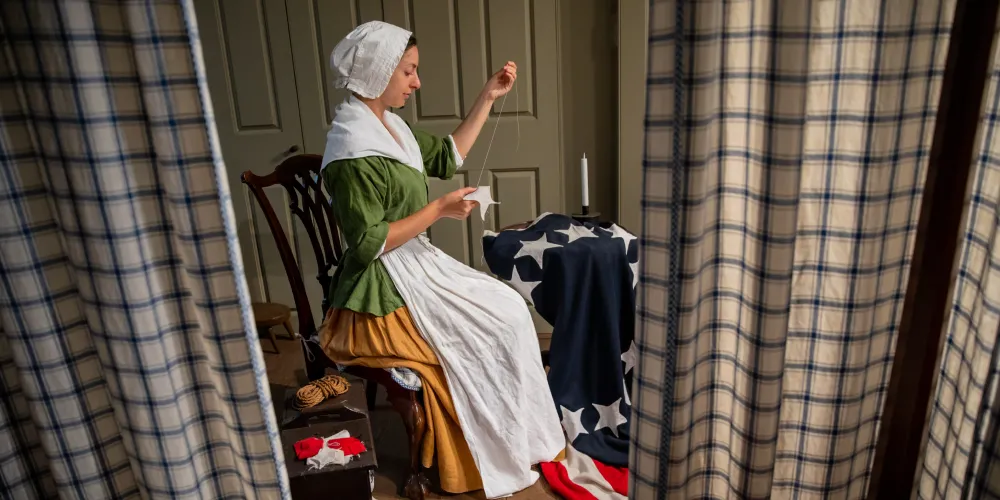 A History Maker portraying Betsy Ross sews the early US flag