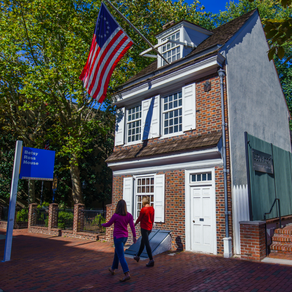 The front exterior of the Betsy Ross House on a sunny day, with the American Flag hanging from the second story window