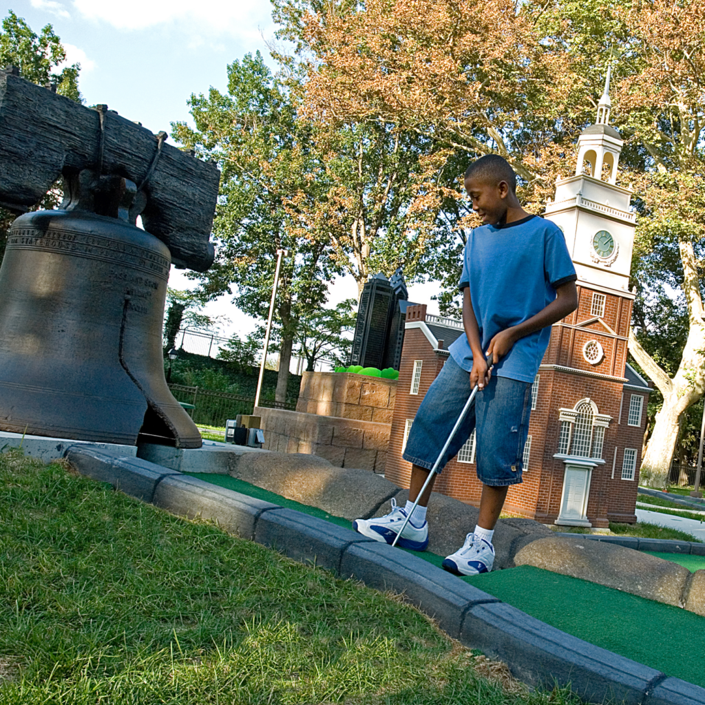 Un niño pone una pelota en una réplica de la Campana de la Libertad en uno de los hoyos en Philly Mini Golf en Franklin Square