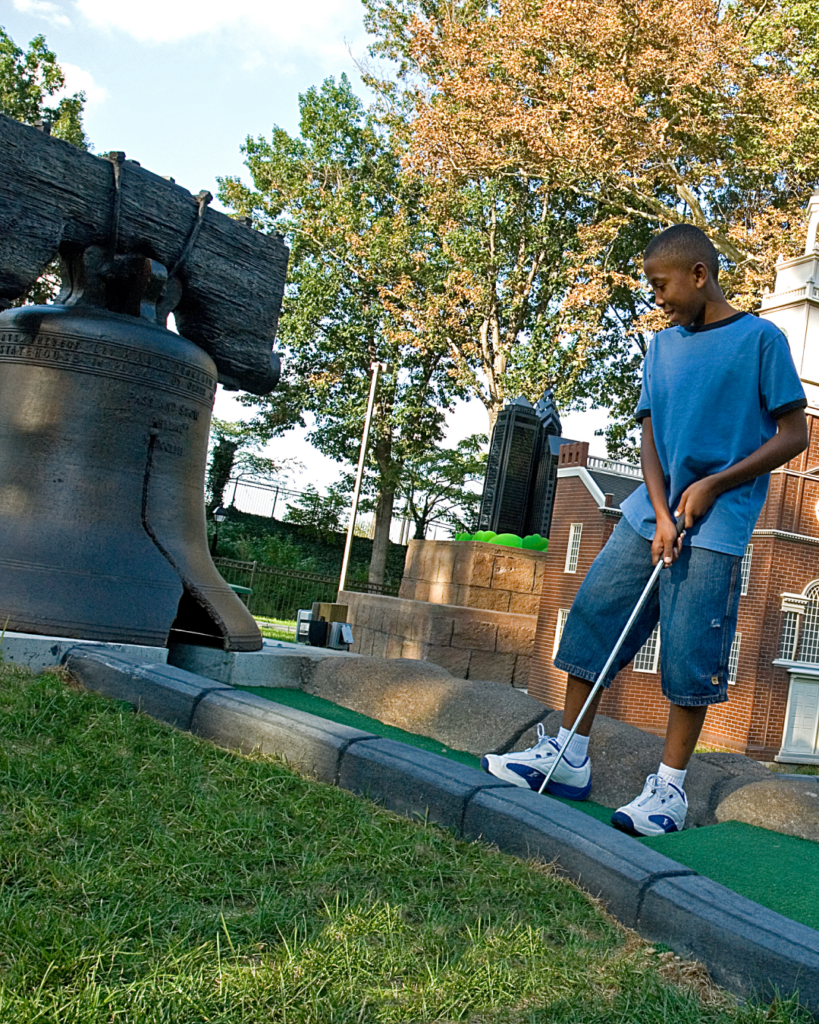A boy putts a golf ball into a replica of the Liberty Bell on the Philly Mini Golf course at Franklin Square