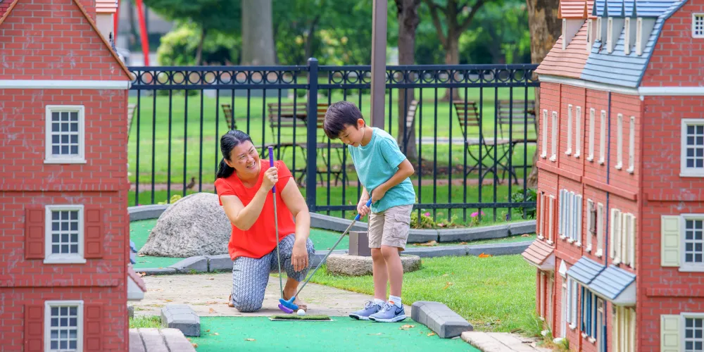 A boy putts a ball on a hole at Franklin Square Philly Mini Golf, with replicas of Philadelphia landmarks