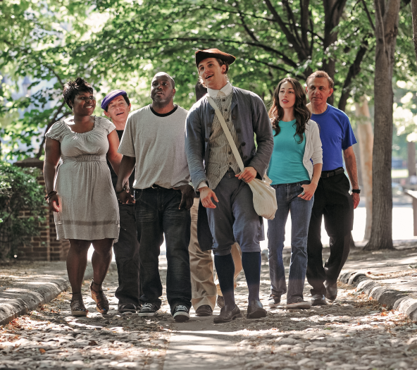 A History Maker in colonial costume leads a walking tour on a cobblestone street in Philadelphia's historic district