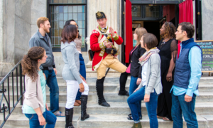 A tour group listens to a History Maker in colonial soldier costume tell a story before entering a tour location