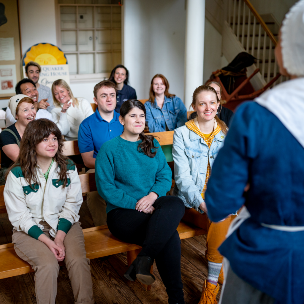 A group of people sit in benches as a History Maker shares stories at the Free Quaker Meeting House