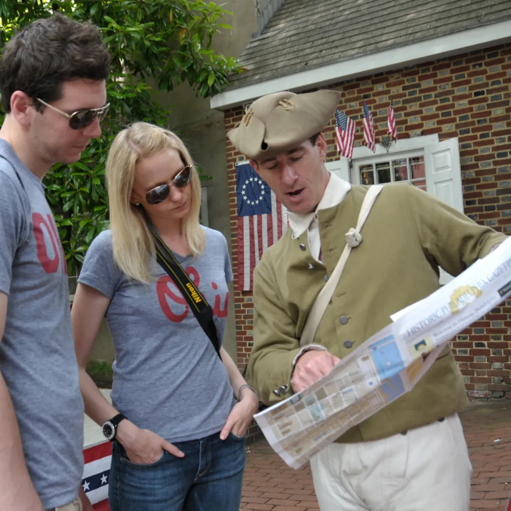 A costumed Once Upon A Nation History Maker shows visitors information in a printed guide called The Gazette