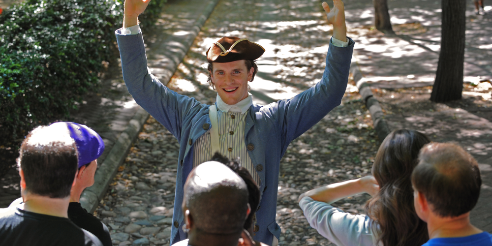 A costumed History Maker leads a tour group on a cobblestone street