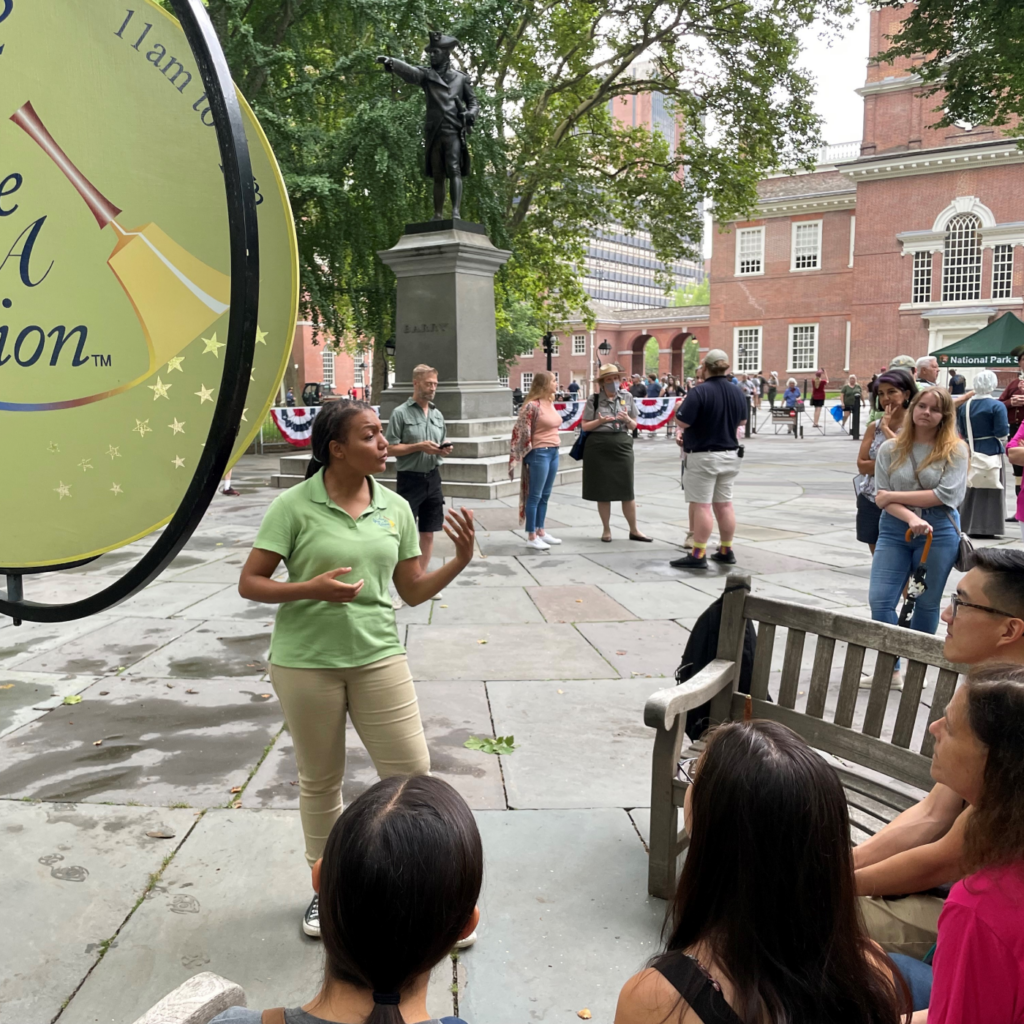 A Once Upon A Nation Storyteller engages a group at one of the curved storytelling benches near Independence Hall