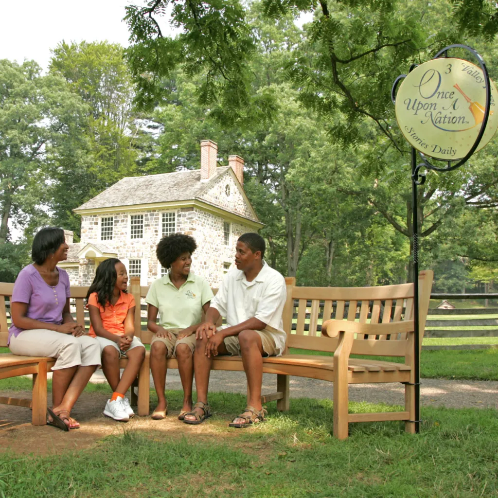 A family sits on a storytelling bench in Valley Forge to listen to a Storyteller tell a story