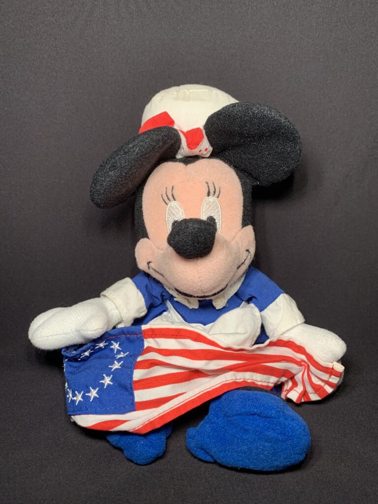 以贝特西·罗斯为原型的米妮毛绒玩具。 她身穿红白蓝相间的衣服，手持十三星旗。