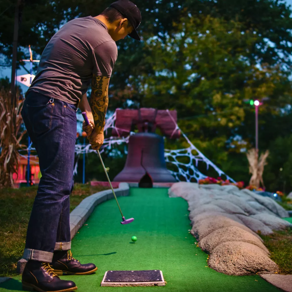 Photo of a man putting into a replica of the liberty bell on the Spooky Philly Mini Golf Course in Franklin Square.